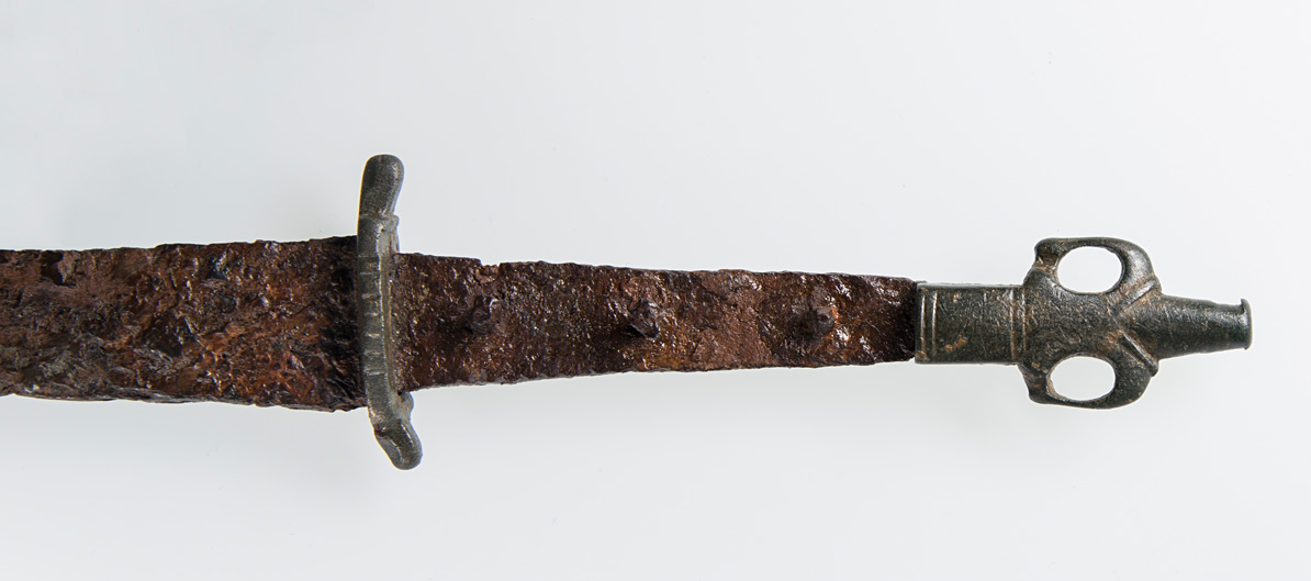 Dieses Dolchmesser stammt aus dem 12./13. Jahrhundert. Das Knaufende könnte als Darstellung einer Person mit in die Hüfte gestemmten Armen gedeutet werden.