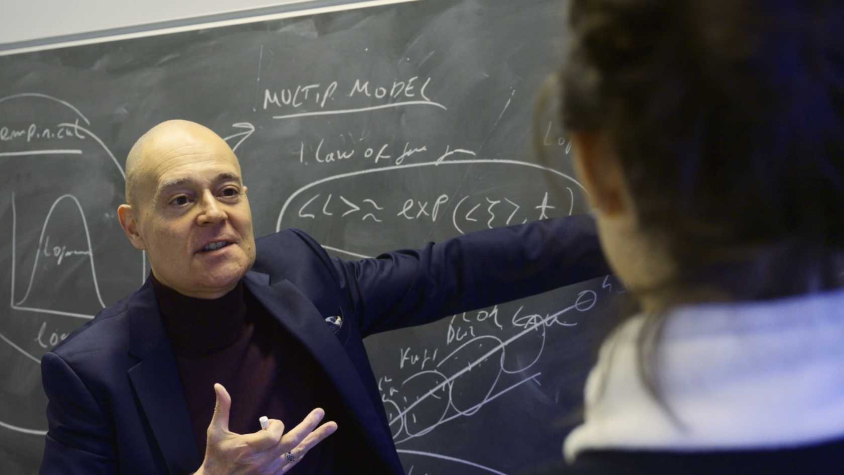 Jordi Bascompte zeigt auf eine Wandtafel voll mit mathematischen Formeln.