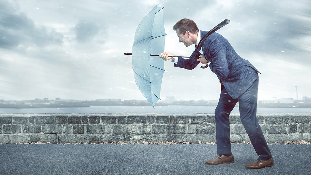 Businessmann mit Schirm gegen den Wind kämpfend