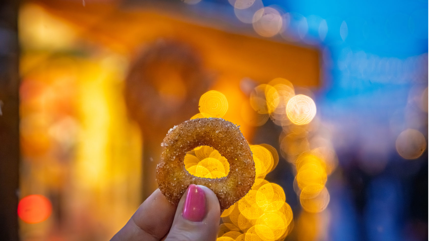 A woman holds up a mini-donut against Christmas market lighting