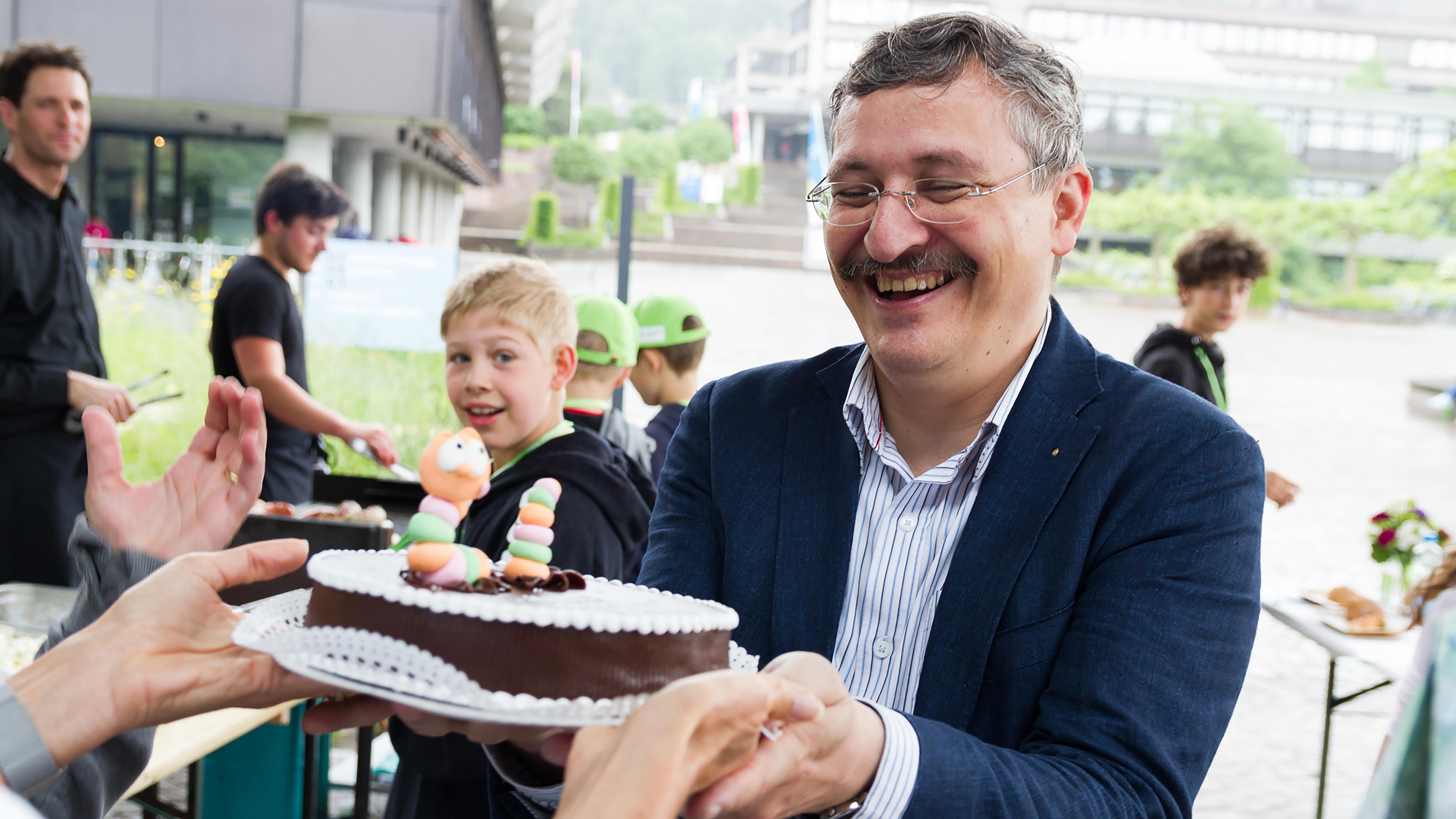 Happy Birthday! Michael Hengartner erhält im Juni 2016 an der Veranstaltung Alumni & Family eine Torte zum 50. Geburtstag. Der lachende Wurm spielt auf seine Erfolge als Molekularbiologe an: Anhand des Fadenwurms Caenorhabditis elegans erforschte Hengartner, welche Mechanismen dazu führen, dass sich beispielsweise eine Zelle mit beschädigtem Erbgut selber tötet und warum dieser Mechanismus bei Krebszellen oft nicht mehr funktioniert. 2006 erhielt er dafür den renommierten Latsis-Preis.