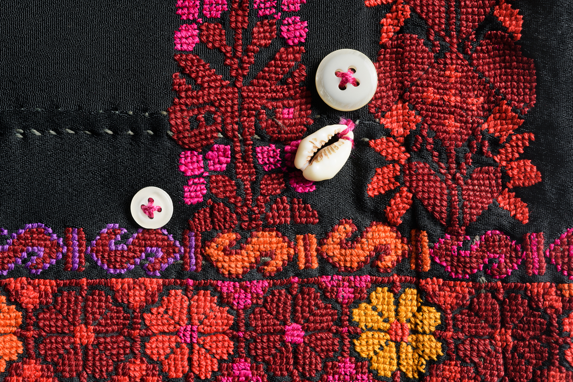 Close-up of buttons and cowry shells that decorate a colorfully embroidered women's jacket. Region of origin: Negev, 1950s.