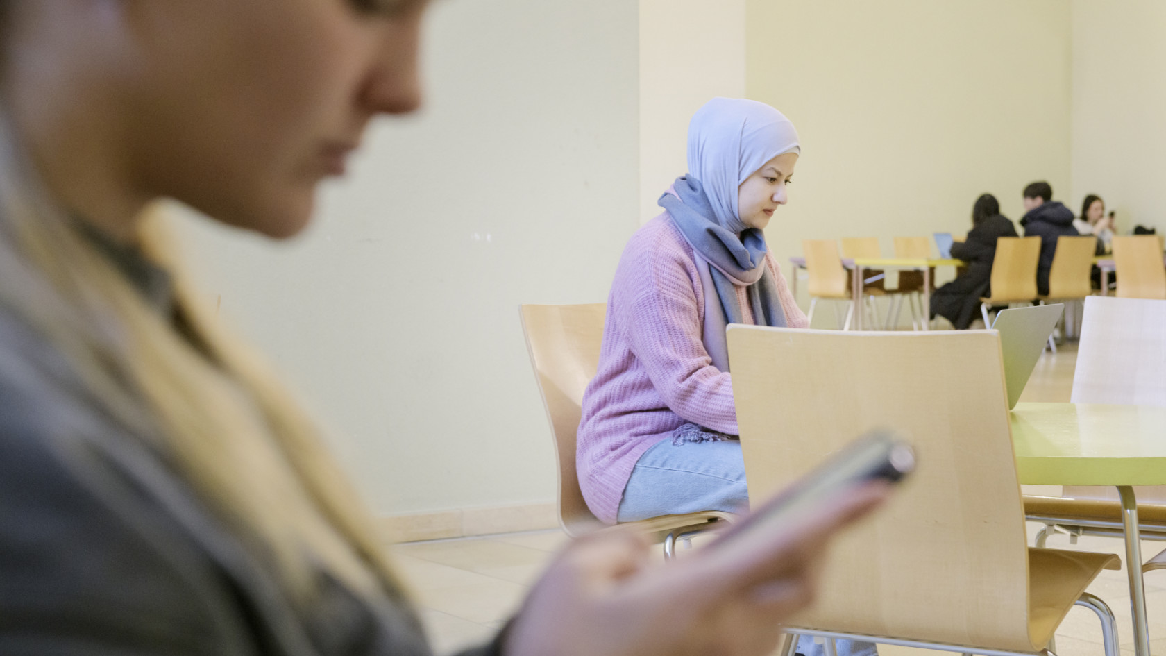 Participant in the Explore program wearing a pink sweater and light blue headscarf sitting at a table with a laptop