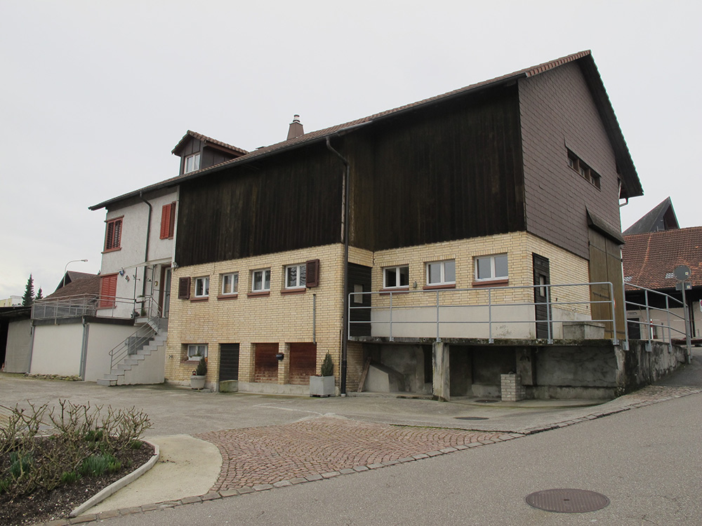 This farmhouse was built in 1940 in the middle of the village – at a time when farmhouses were almost exclusively constructed outside villages. It replaced a farmhouse that had burnt down. The relatively modern design of the house is reminiscent of the multi-purpose design of traditional farmhouses with living and working areas under one roof. The barns are not at right angles to the house as is usual, however, but are situated lengthwise continuing the roof ridge with the entrance on the front end. The barn also has south-facing windows which let a lot of light in, giving a modern light and airy feel. (image used with permission)