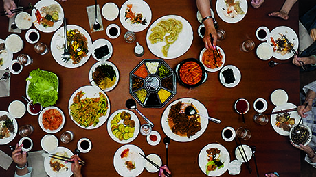 Das Bild aus dem Film zur Ausstellung S(e)oul food zeigt essende Menschen an einem reich gedeckten Tisch.