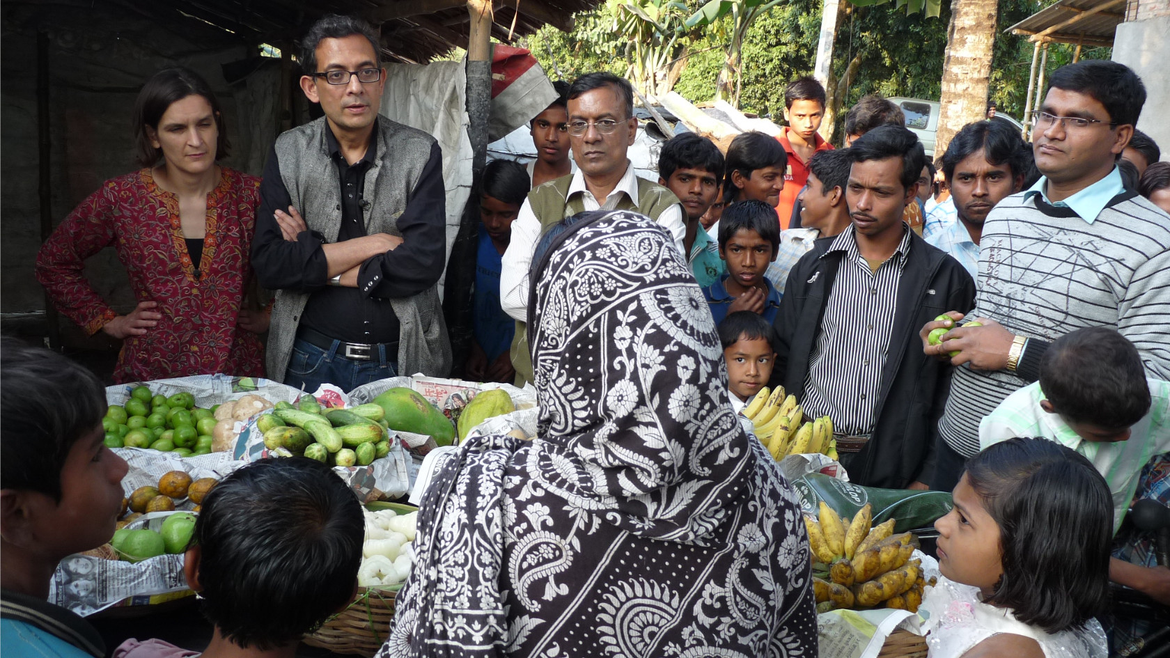 Esther Duflo and Abhijit Banerjee surrounded by people with fruit on display in India.