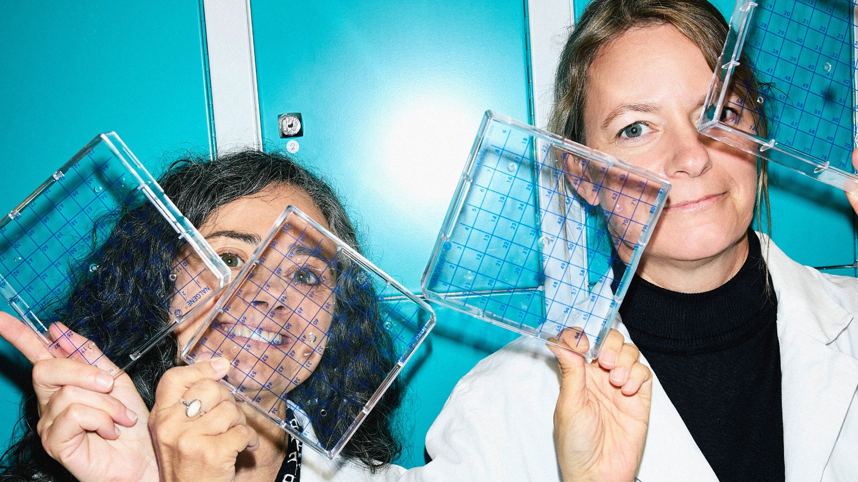 Die beiden Forschenden Mireia Sospedra und Nicole Joller, die durchsichtige Zellkulturplatten hochhalten 