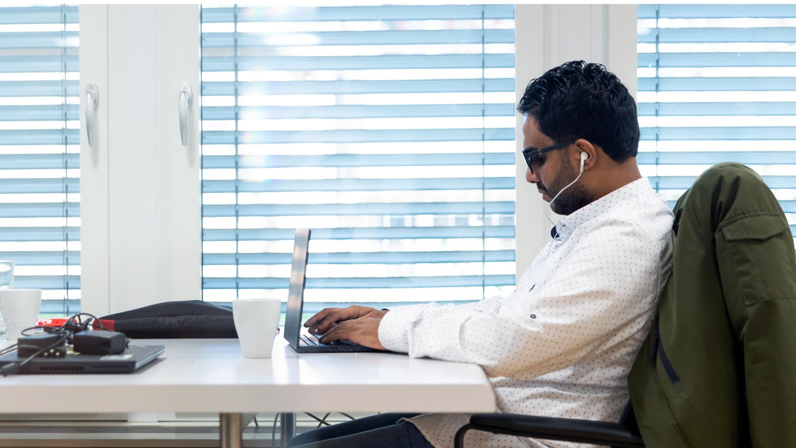 Mo Sherif sits in front of his laptop wearing sunglasses and headphones