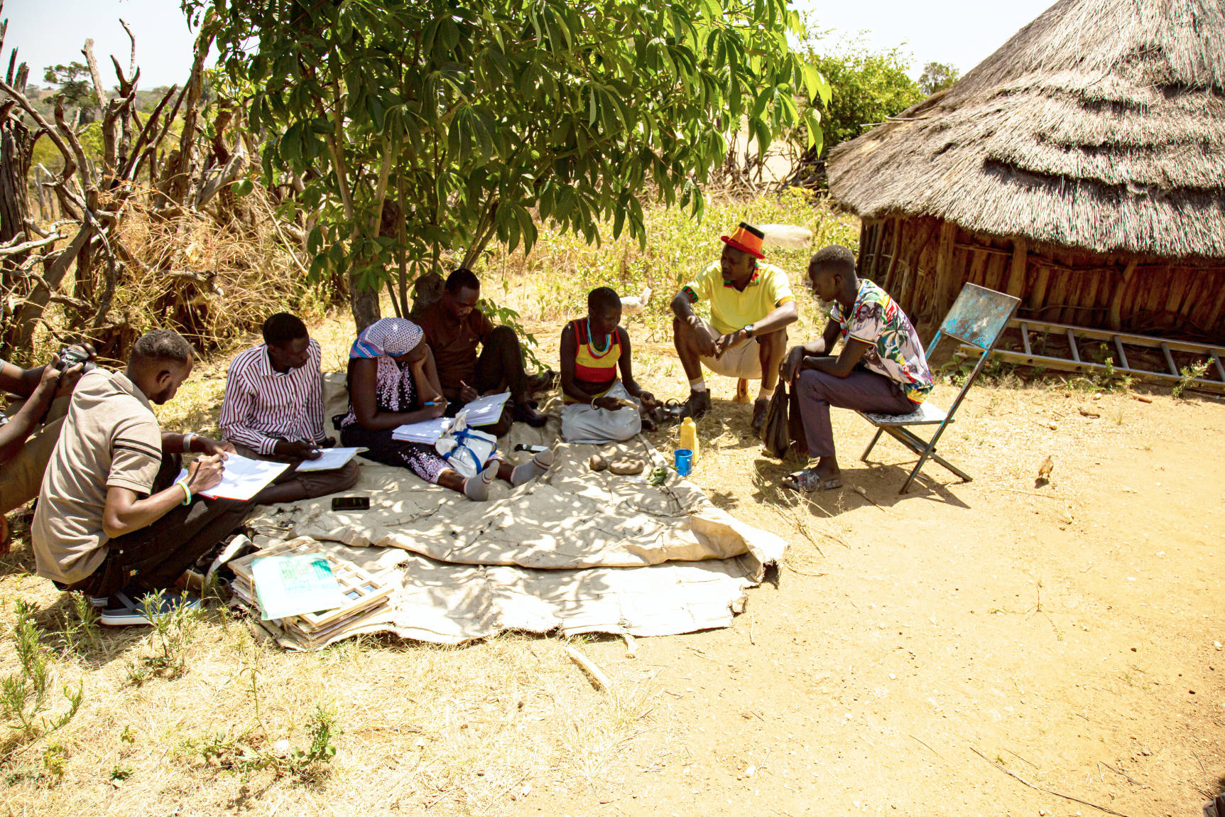 Mitglieder des transdisziplinären Forschungsteams der Makerere-Universität und des Uganda National Museum bei der Feldarbeit in Kaabong, im Nordosten von Uganda. Sie sprechen mit einer lokalen Heilerin und Heilpflanzenkundigen der Ik über deren Heilpflanzenwissen. Dazu arbeiten sie mit einem Übersetzer.