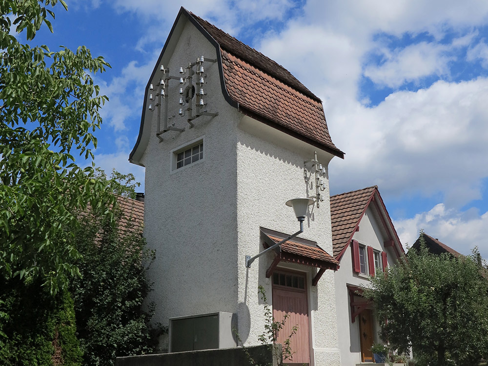 This little tower in Weiach from 1910 is one of the few remaining electricity substations in the Dielsdorf district. At the start of the 20th century, when Switzerland first got electricity, these types of buildings began to spring up. Their design is very varied, for example historicist brick constructions or the refined styles of Art Nouveau or Heimatstil. The building in Weiach has an undulating mansard pitched roof, a typical feature of Heimatstil harking back to preindustrial construction traditions. (image used with permission)