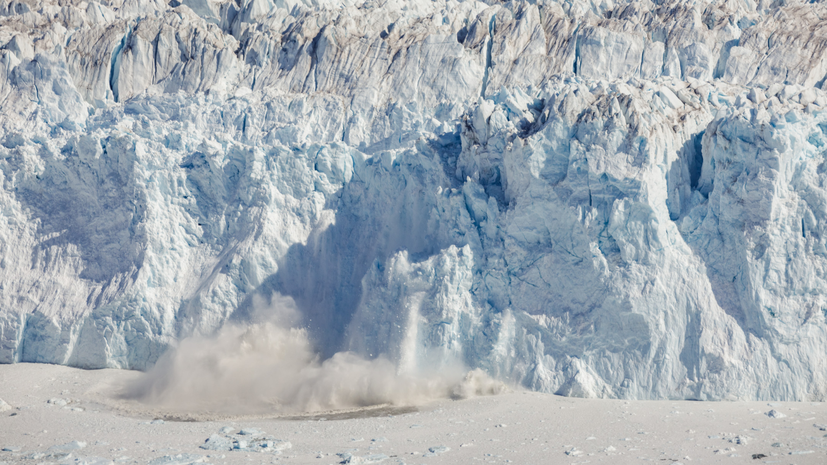 An ice tower breaks off from the 80-meter-high ice front of the calving Eqalorutsit Kangilliit Sermiat glacier in southern Greenland. The impact creates a large tsunami wave on the ocean surface.